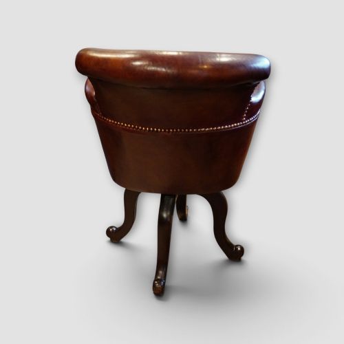 fig 3. An Edwardian mahogany and chestnut brown leather swivel desk chair with a curved tub backrest, brass stud detail, and a carved four-star base.