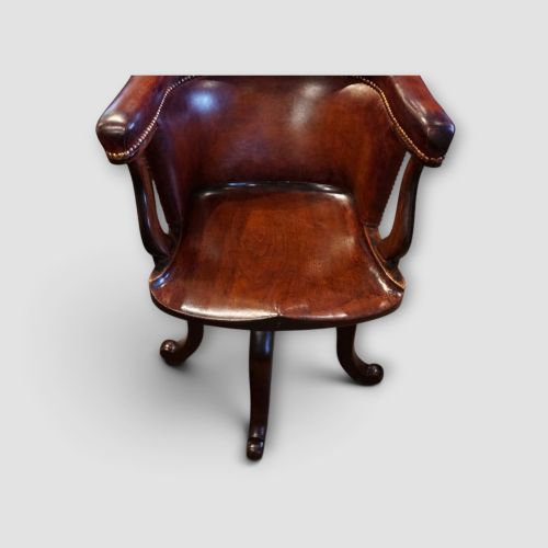 fig 4. An Edwardian mahogany and chestnut brown leather swivel desk chair with a curved tub backrest, brass stud detail, and a carved four-star base.