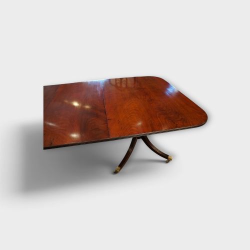 fig 1. A Georgian style dark mahogany dining table featuring an extendable top, twin turned pedestal pillars, and splayed quadruped legs with brass toe caps.