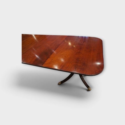 fig 3. A Georgian style dark mahogany dining table featuring an extendable top, twin turned pedestal pillars, and splayed quadruped legs with brass toe caps.