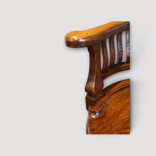 fig 1. An Edwardian dark oak revolving desk chair featuring a curved slatted backrest, shaped wooden saddle seat, and four legs with castors.