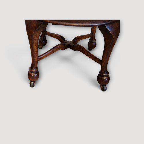 fig 4. An Edwardian dark oak revolving desk chair featuring a curved slatted backrest, shaped wooden saddle seat, and four legs with castors.