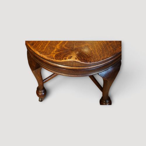 fig 5. An Edwardian dark oak revolving desk chair featuring a curved slatted backrest, shaped wooden saddle seat, and four legs with castors.