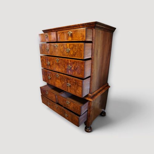 fig 5. An antique Queen Anne walnut chest-on-chest in two sections featuring a multi-drawer configuration, figured grain patterns, brass drop handles, and bun feet.