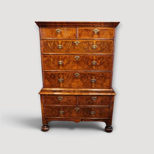 fig 6. An antique Queen Anne walnut chest-on-chest in two sections featuring a multi-drawer configuration, figured grain patterns, brass drop handles, and bun feet.