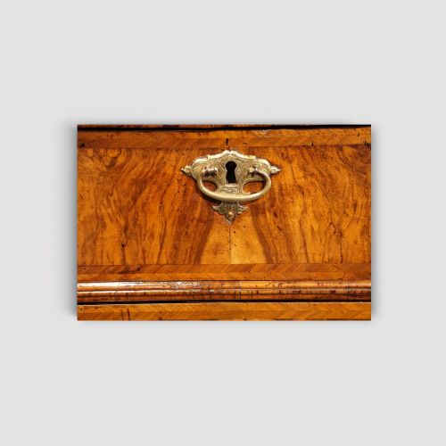 fig 7. An antique Queen Anne walnut chest-on-chest in two sections featuring a multi-drawer configuration, figured grain patterns, brass drop handles, and bun feet.