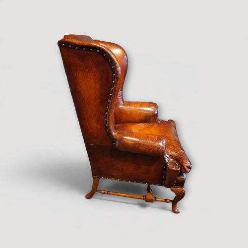 fig 9. A pair of brown leather Queen Anne style wingback armchairs featuring deep seat cushions, brass stud detailing, and carved walnut cabriole legs.