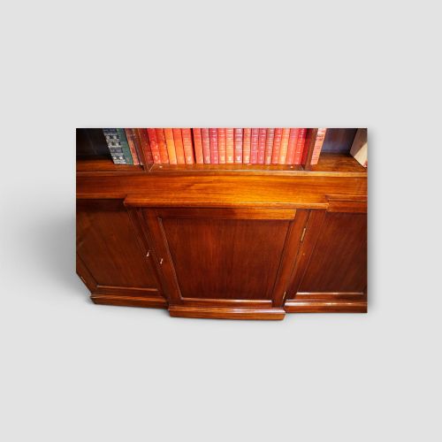 fig 3. An Edwardian mahogany breakfront bookcase featuring an open upper shelving section filled with books and an enclosed lower cupboard base.