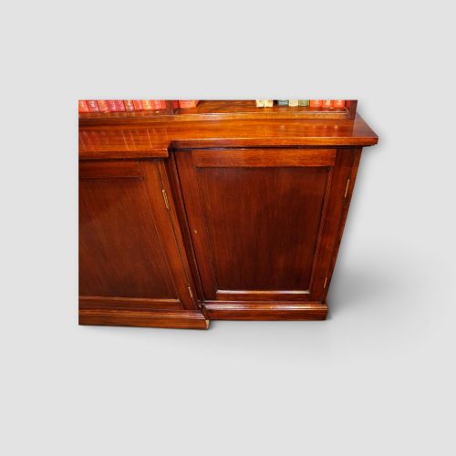 fig 8. An Edwardian mahogany breakfront bookcase featuring an open upper shelving section filled with books and an enclosed lower cupboard base.
