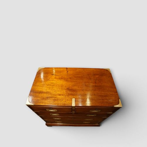 fig 7. A wooden chest of drawers featuring brass corner brackets, flush handles, and two short drawers above three long drawers.