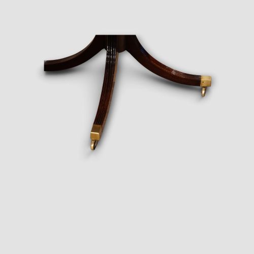 fig 3. An extended mahogany twin pedestal dining table featuring a polished surface, rounded corners, reeded tripod legs, and brass castors.