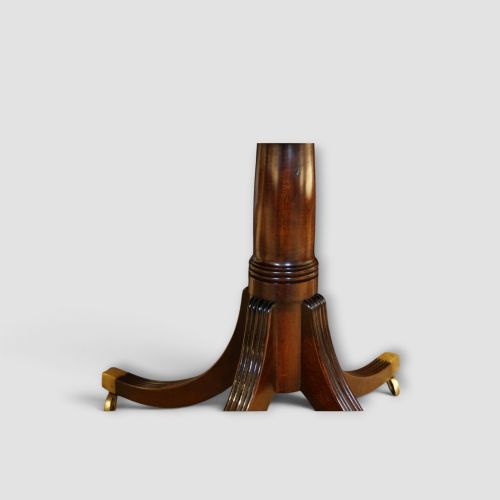 fig 4. An extended mahogany twin pedestal dining table featuring a polished surface, rounded corners, reeded tripod legs, and brass castors.
