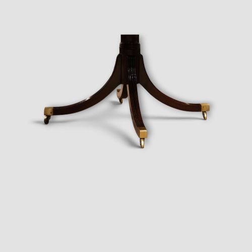 fig 7. An extended mahogany twin pedestal dining table featuring a polished surface, rounded corners, reeded tripod legs, and brass castors.