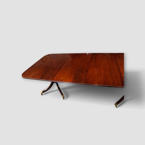 fig 8. An extended mahogany twin pedestal dining table featuring a polished surface, rounded corners, reeded tripod legs, and brass castors.