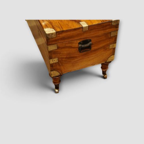fig 2. A low rectangular warm amber camphor wood campaign trunk featuring brass strap corners, flush brass handles, dual keyholes, and turned legs with castors.