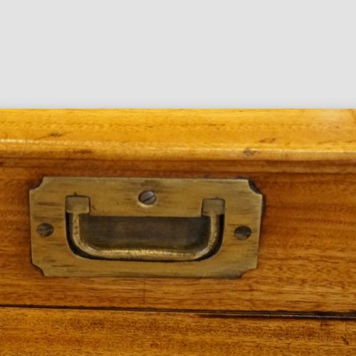 fig 7. A low rectangular warm amber camphor wood campaign trunk featuring brass strap corners, flush brass handles, dual keyholes, and turned legs with castors.