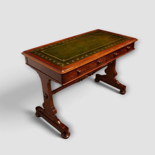 fig 1. An early Victorian mahogany writing table featuring a green leather inset top with gilt tooling, two frieze drawers, a turned stretcher, and end supports.