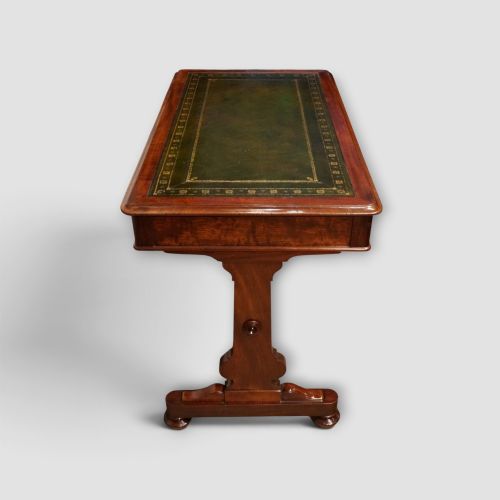 fig 6. An early Victorian mahogany writing table featuring a green leather inset top with gilt tooling, two frieze drawers, a turned stretcher, and end supports.