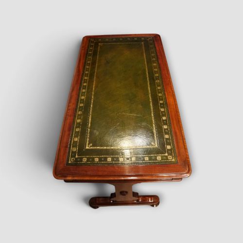 fig 8. An early Victorian mahogany writing table featuring a green leather inset top with gilt tooling, two frieze drawers, a turned stretcher, and end supports.