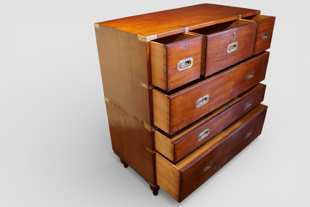 A Victorian teak military campaign chest featuring brass corner bindings, flush recessed brass handles, turned feet, and a two-part carcass construction. View VI