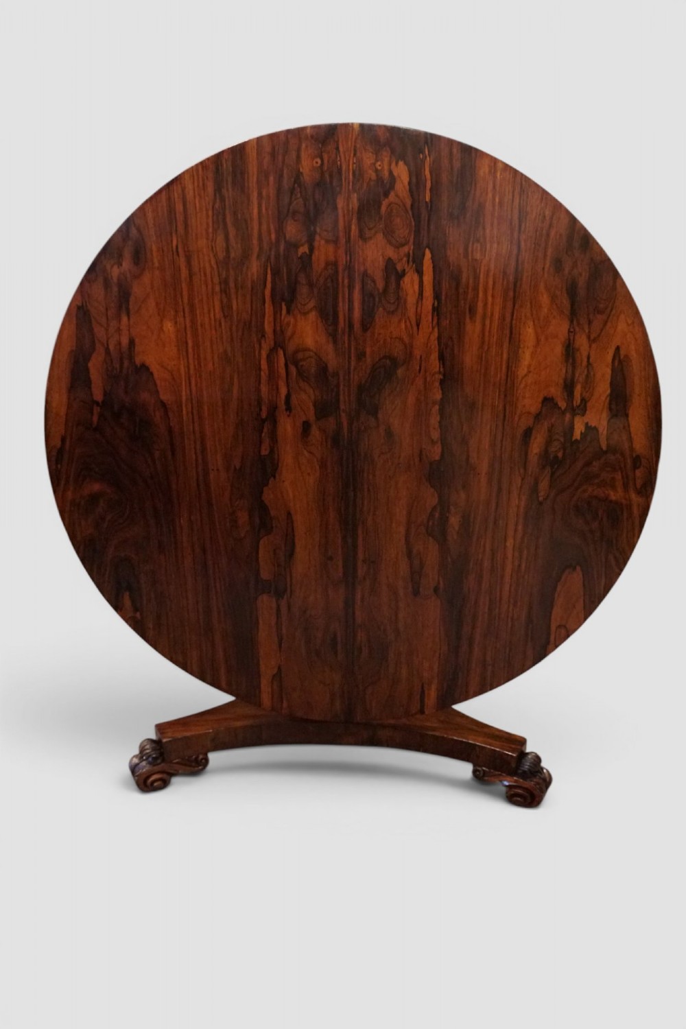 A circular William IV rosewood dining table with a figured veneer top on a central pedestal and tripartite base with scroll feet. View V