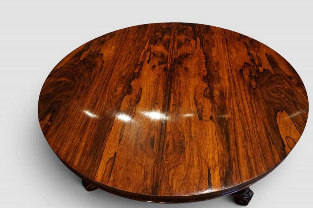 A circular William IV rosewood dining table with a figured veneer top on a central pedestal and tripartite base with scroll feet. View VI