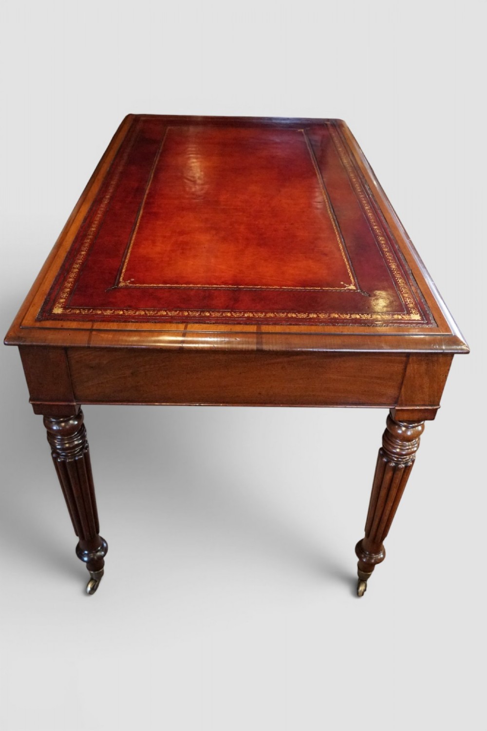 A Victorian mahogany partners writing table with a red leather gold-tooled insert top, frieze drawers, turned reeded legs, and brass castors. View VI