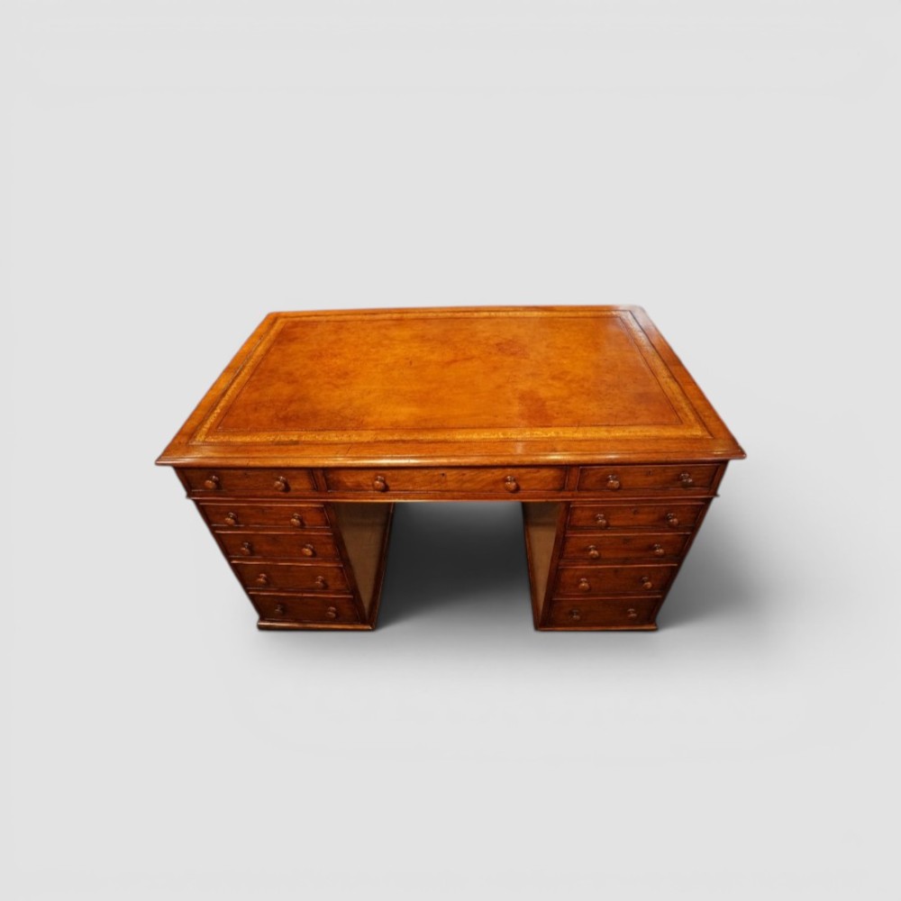 A Victorian mahogany partners desk featuring a tooled leather writing surface, twin pedestals, and an eleven-drawer front configuration with turned wooden knobs.