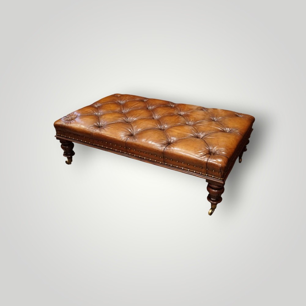 A large rectangular deep-buttoned tan leather Chesterfield footstool featuring brass stud trim, turned timber legs, and brass castors. View II