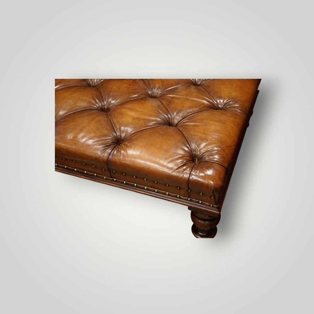 A large rectangular deep-buttoned tan leather Chesterfield footstool featuring brass stud trim, turned timber legs, and brass castors. View IV