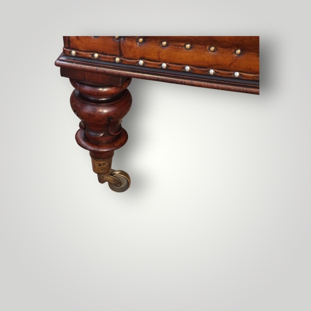 A large rectangular deep-buttoned tan leather Chesterfield footstool featuring brass stud trim, turned timber legs, and brass castors. View VII
