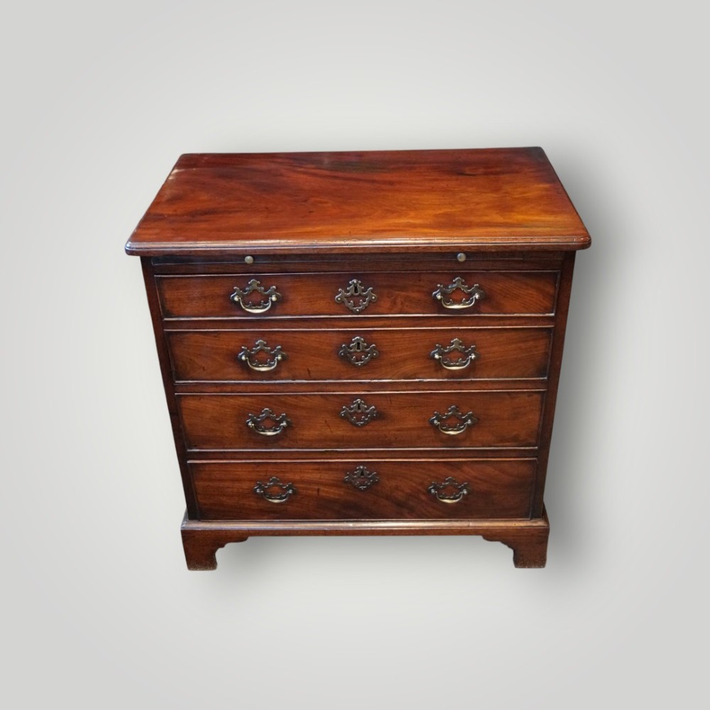 A compact George III mahogany bachelors chest featuring four graduated drawers, brass handles, a pull-out brushing slide, and bracket feet.