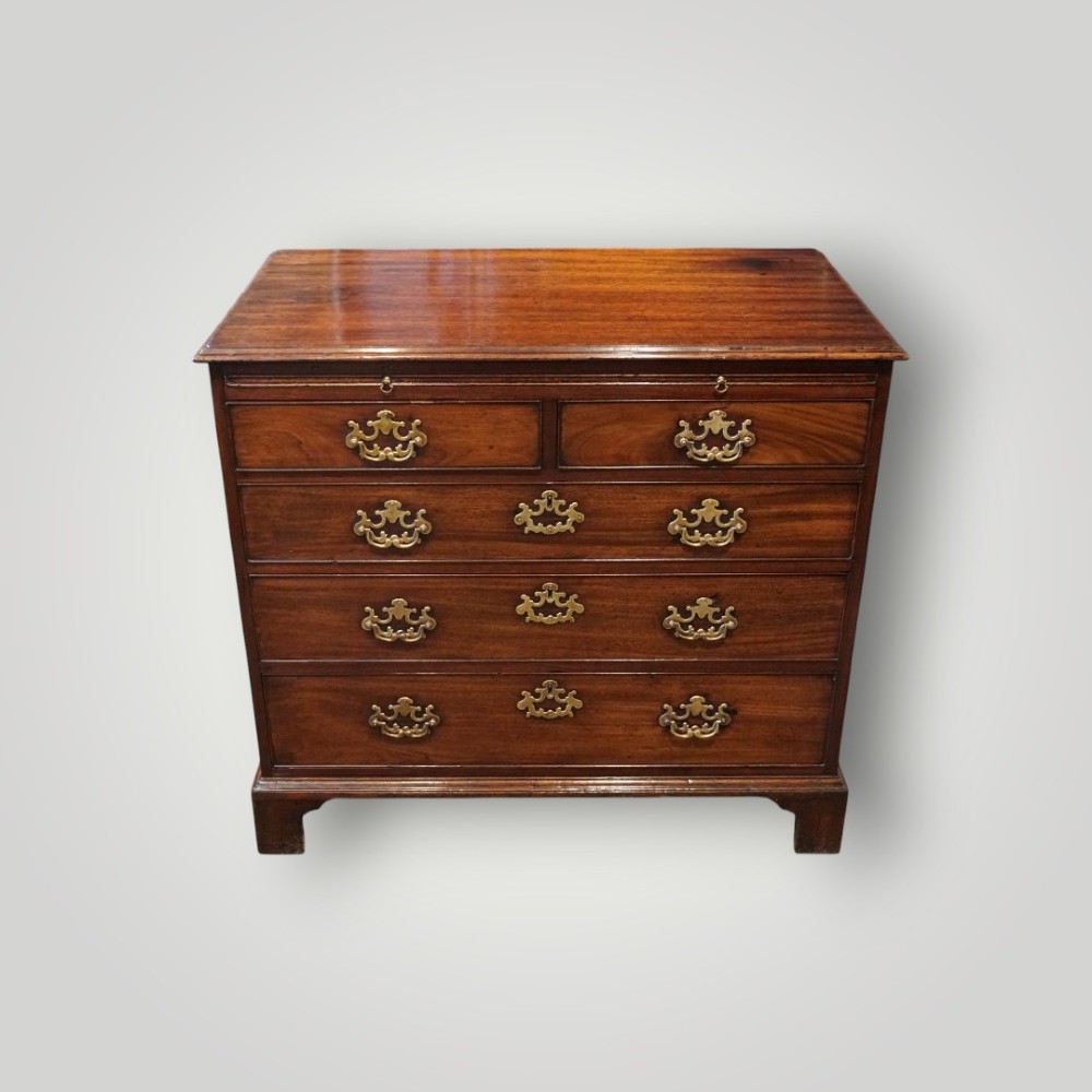 A George III mahogany bachelors chest featuring a top brushing slide, graduated drawers with pierced brass handles, and bracket feet.