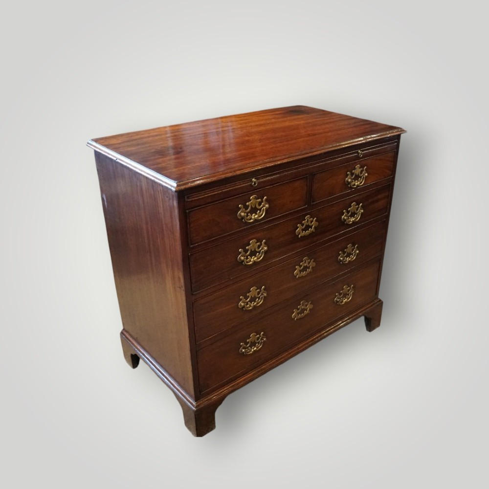 A George III mahogany bachelors chest featuring a top brushing slide, graduated drawers with pierced brass handles, and bracket feet. View II