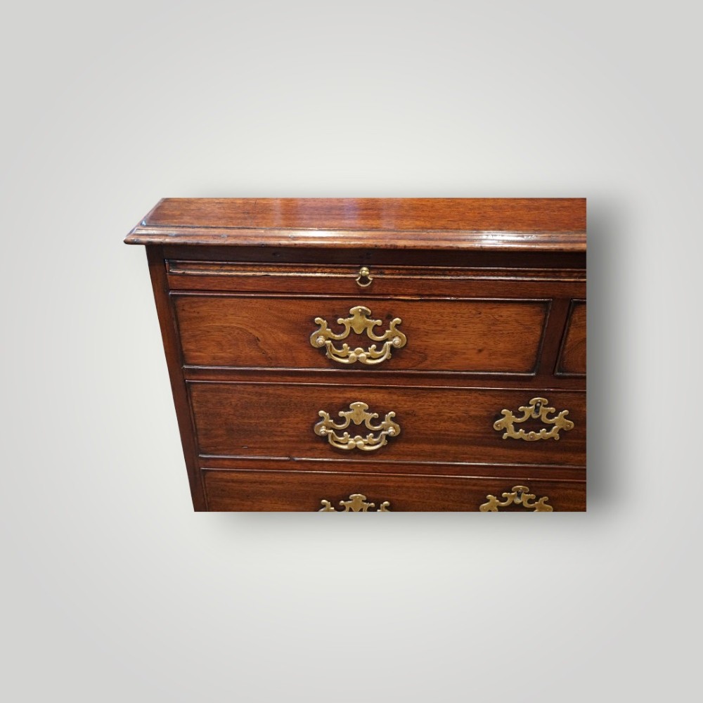 A George III mahogany bachelors chest featuring a top brushing slide, graduated drawers with pierced brass handles, and bracket feet. View IV
