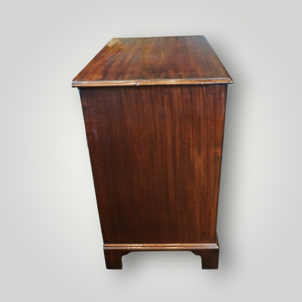 A George III mahogany bachelors chest featuring a top brushing slide, graduated drawers with pierced brass handles, and bracket feet. View V