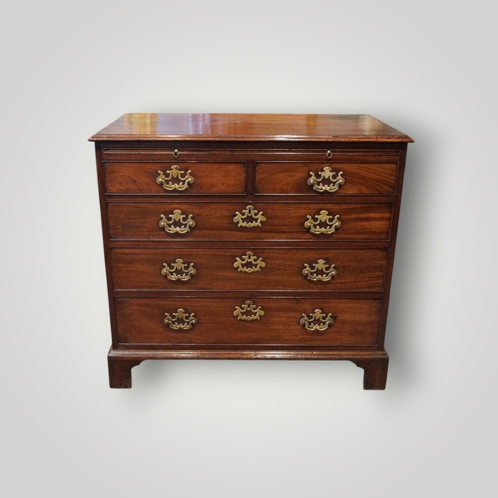 A George III mahogany bachelors chest featuring a top brushing slide, graduated drawers with pierced brass handles, and bracket feet. View VI
