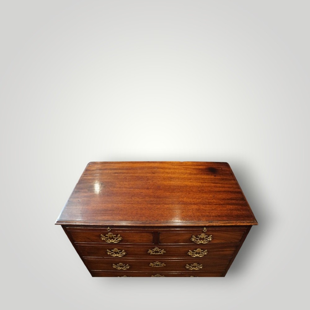 A George III mahogany bachelors chest featuring a top brushing slide, graduated drawers with pierced brass handles, and bracket feet. View X