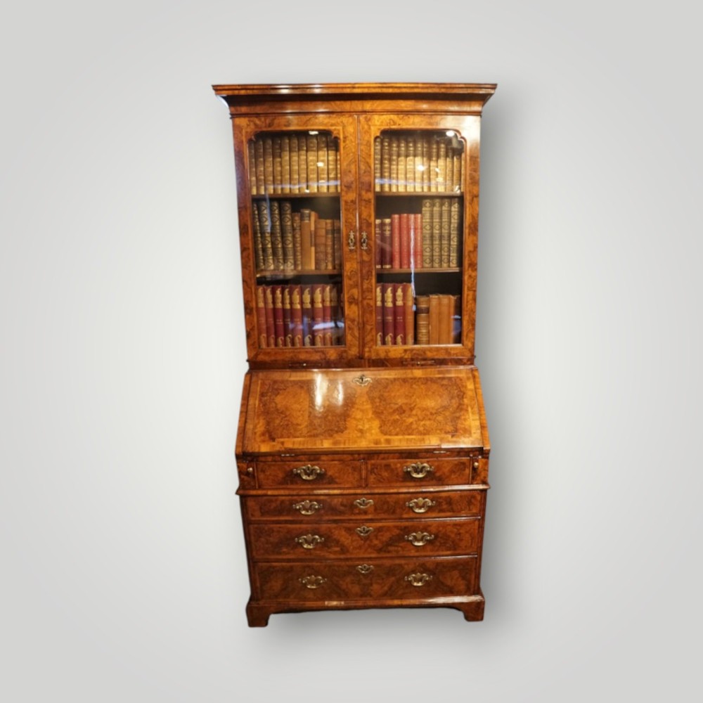A George I walnut bureau bookcase featuring glazed upper doors housing books, a slant-front writing flap, and lower drawers with brass drop handles.