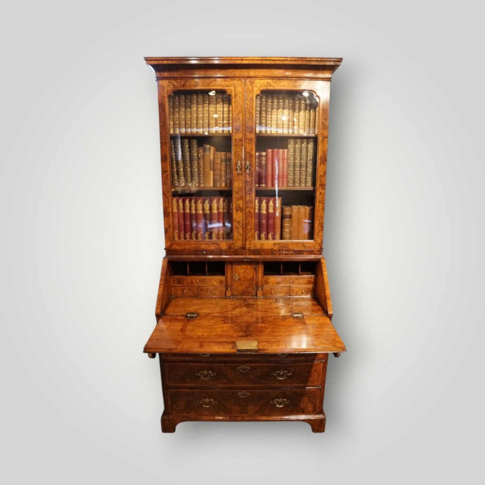 A George I walnut bureau bookcase featuring glazed upper doors housing books, a slant-front writing flap, and lower drawers with brass drop handles. View II