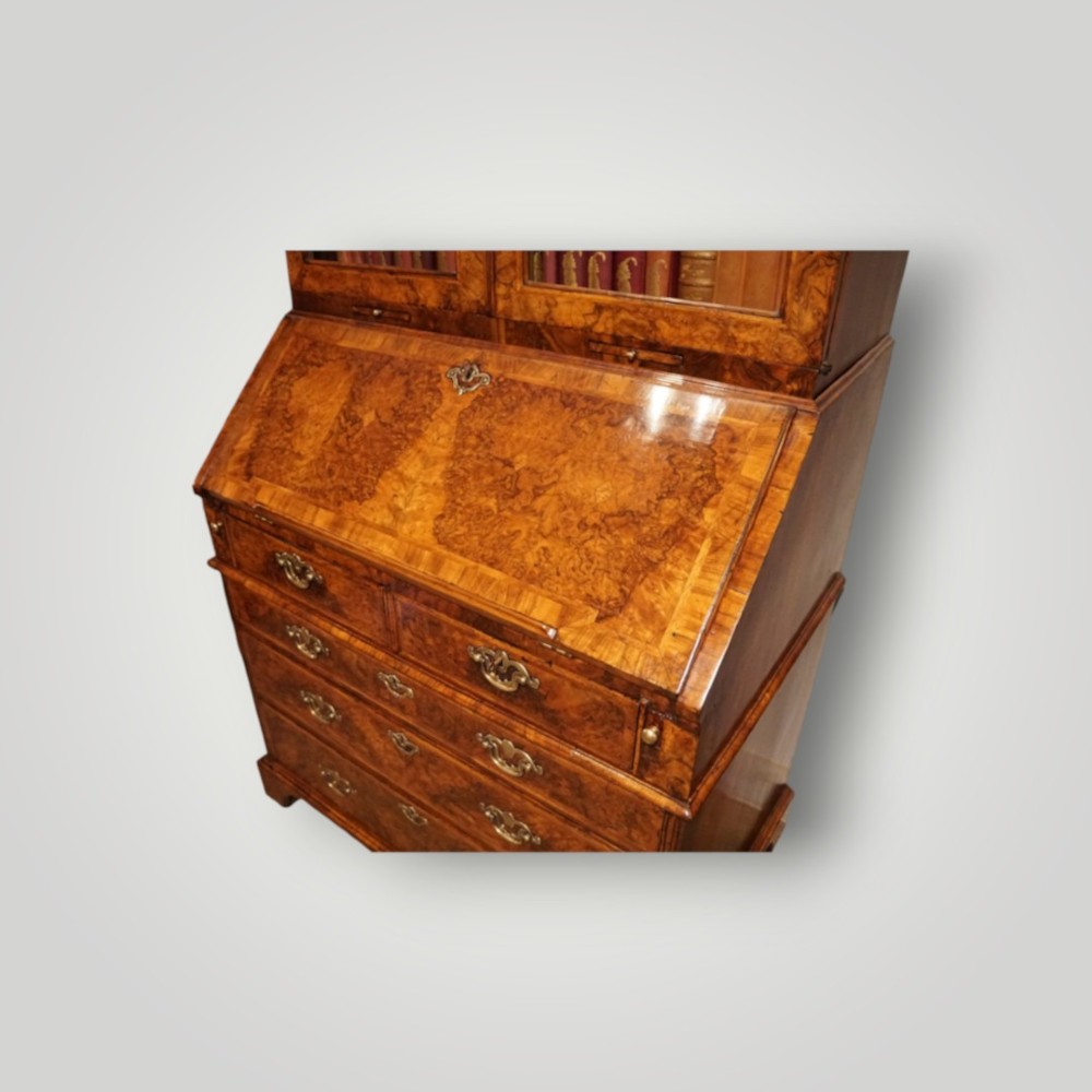 A George I walnut bureau bookcase featuring glazed upper doors housing books, a slant-front writing flap, and lower drawers with brass drop handles. View V