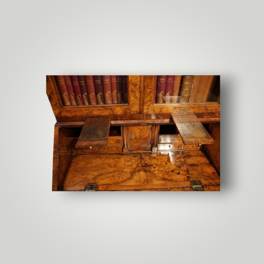 A George I walnut bureau bookcase featuring glazed upper doors housing books, a slant-front writing flap, and lower drawers with brass drop handles. View IX