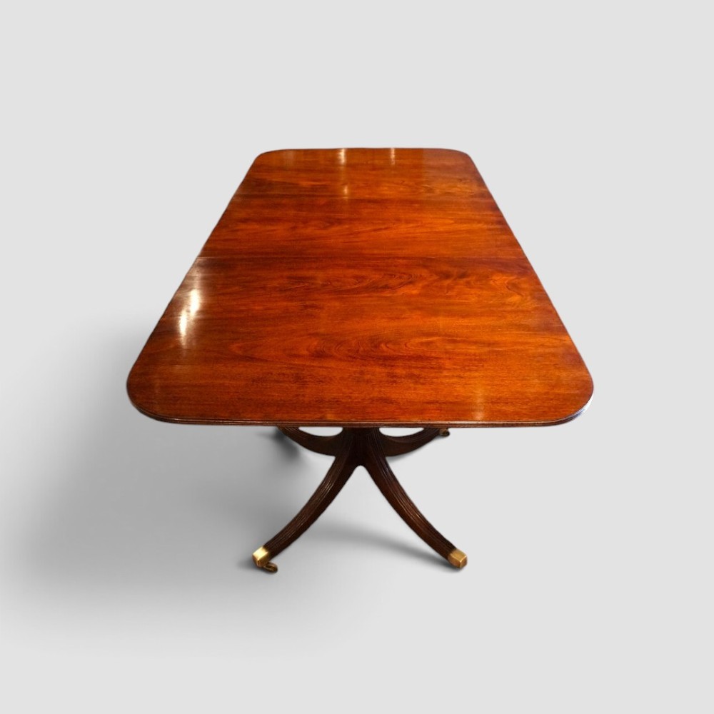 A polished mahogany twin pillar dining table featuring rounded corners, two turned central pedestals, and splayed legs resting on brass castors. View V