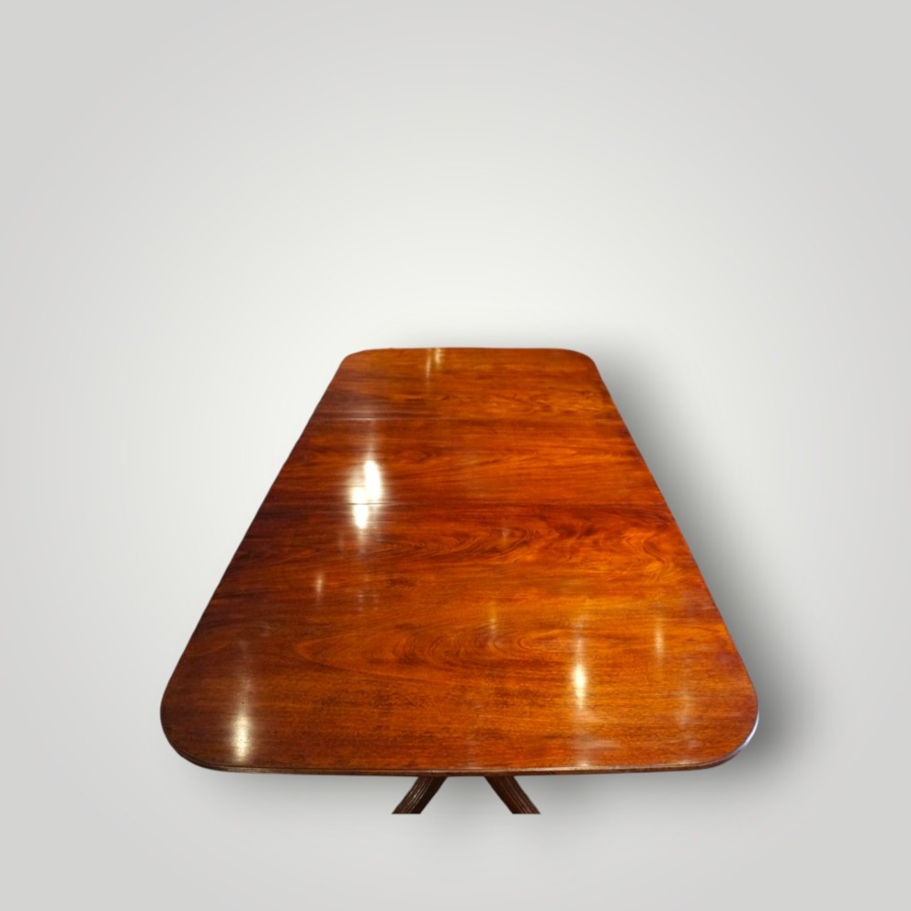 A polished mahogany twin pillar dining table featuring rounded corners, two turned central pedestals, and splayed legs resting on brass castors. View XI