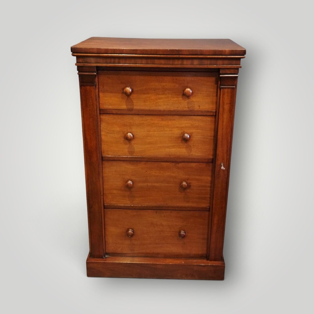 A Victorian warm brown mahogany Wellington chest featuring four stacked drawers with turned wooden handles and a side locking bar. View V