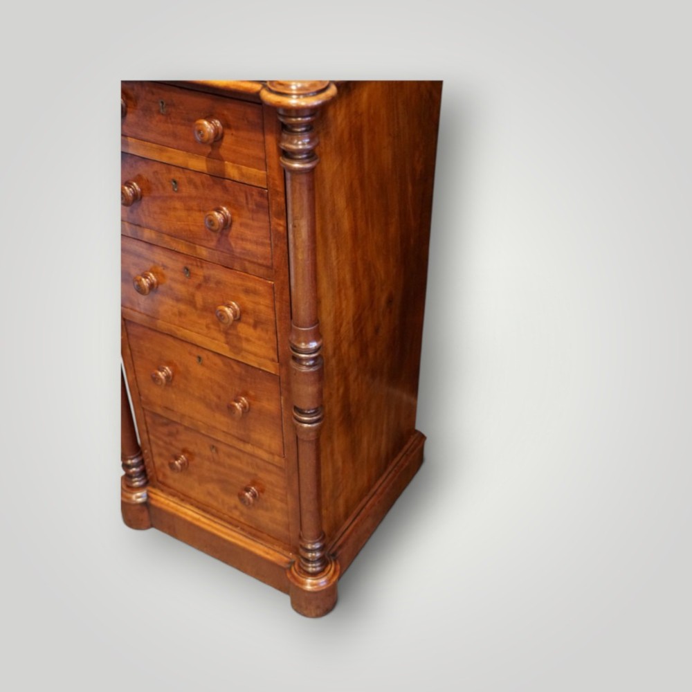 A matching pair of narrow Victorian mahogany bedside chests featuring five graduated drawers with turned side columns on plinth bases. View II