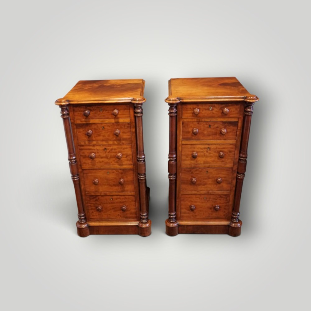 A matching pair of narrow Victorian mahogany bedside chests featuring five graduated drawers with turned side columns on plinth bases. View IV