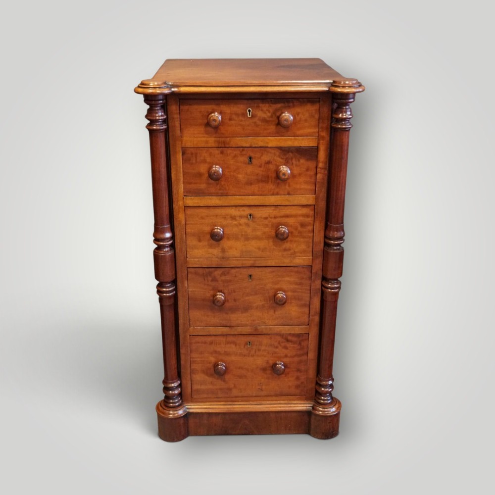 A matching pair of narrow Victorian mahogany bedside chests featuring five graduated drawers with turned side columns on plinth bases. View V