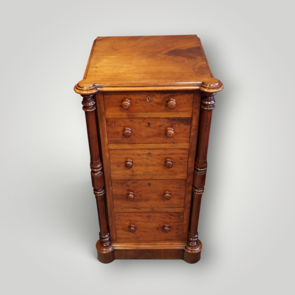 A matching pair of narrow Victorian mahogany bedside chests featuring five graduated drawers with turned side columns on plinth bases. View VIII