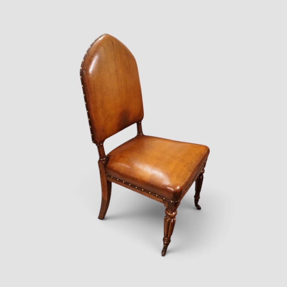 A set of four Victorian oak dining chairs featuring arched gothic-style backrests upholstered in warm brown leather with brass stud trim. View II